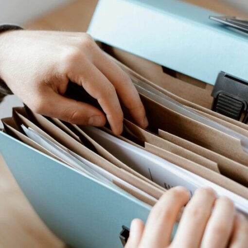 A person sorting through documents in an expanding file organiser with multiple labelled compartments, stored inside a light blue portable filing box.