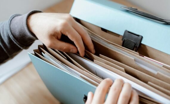 A person sorting through documents in an expanding file organiser with multiple labelled compartments, stored inside a light blue portable filing box.