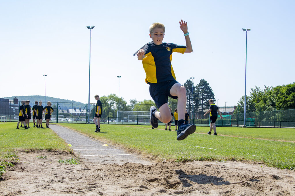 A photo of a Castell Alun student soaring through the air during the High Jump at Sports Day