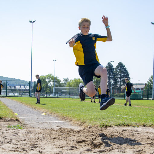 A photo of a Castell Alun student soaring through the air during the High Jump at Sports Day