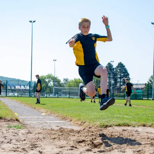A photo of a Castell Alun student soaring through the air during the High Jump at Sports Day