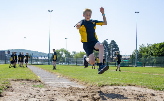 A photo of a Castell Alun student soaring through the air during the High Jump at Sports Day