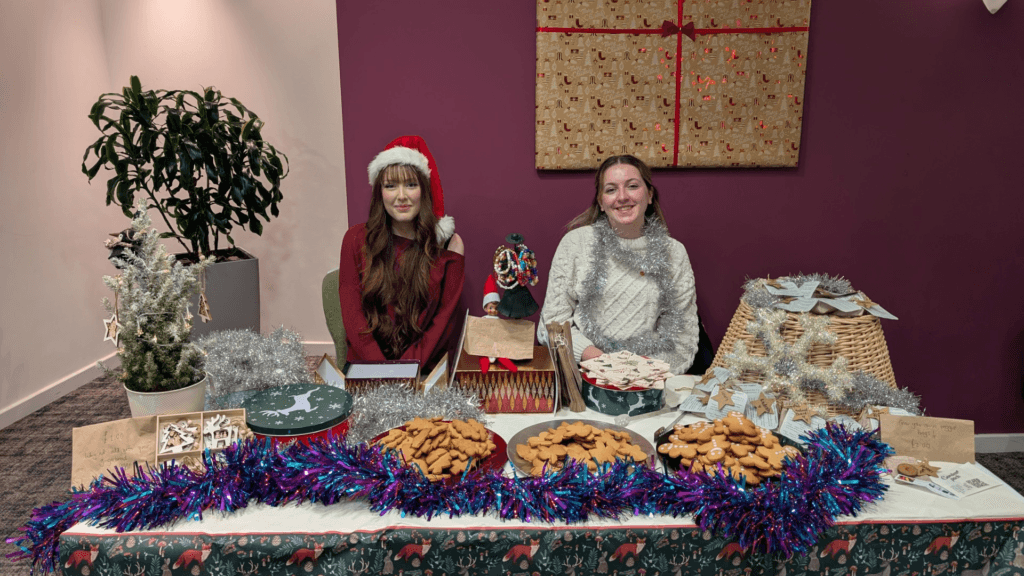 A photograph of two Sixth Form students hosting a Christmas goodies sale at the Ramada Hotel in Wrexham in aid of Hope House Hospice, circa December 2024.