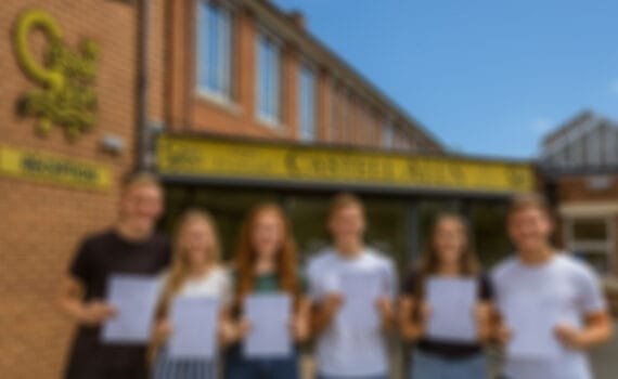 Six students standing outside the entrance to Castell Alun High School, each holding a results sheet while posing for a photograph in front of the school sign and main entrance.