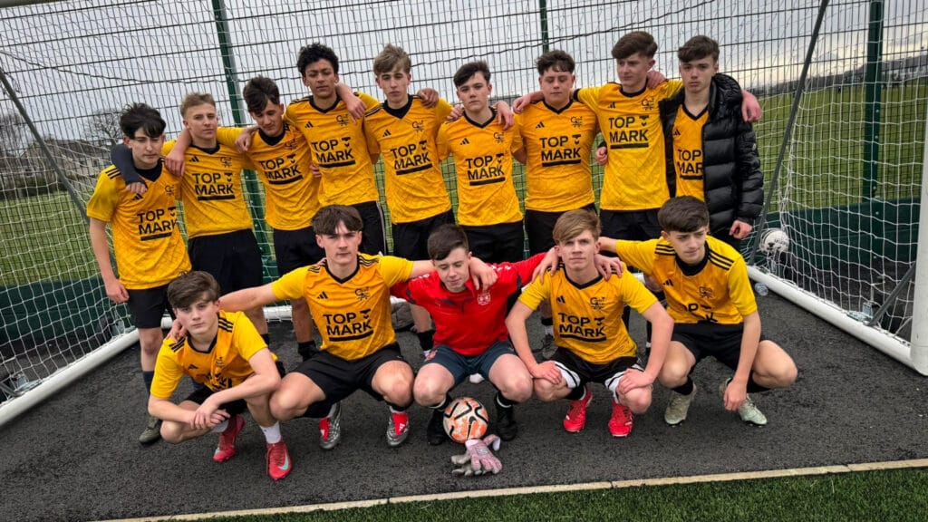 A boys football team group photo on the outdoor pitch, wearing yellow and black kit, circa January 2026