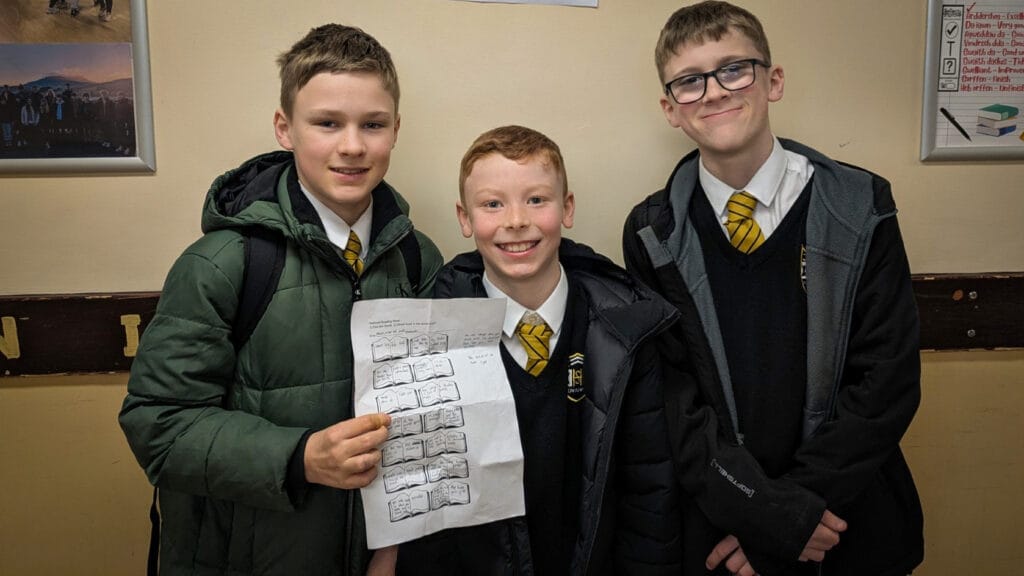 Three students posing in school uniform holding a completed worksheet in a corridor display area, circa January 2026
