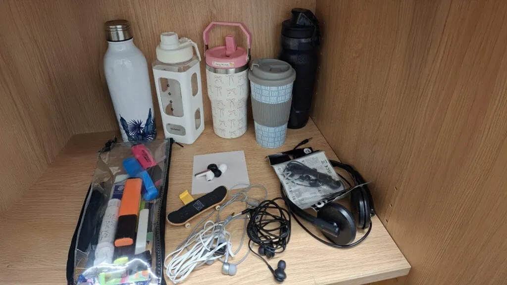 Lost property items on a shelf including water bottles, a pencil case, earphones, and headphones, circa February 2026