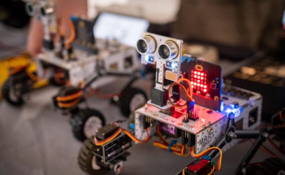 Two small wheeled robots with visible wiring, sensors and LED lights displayed on a table, circa February 2026