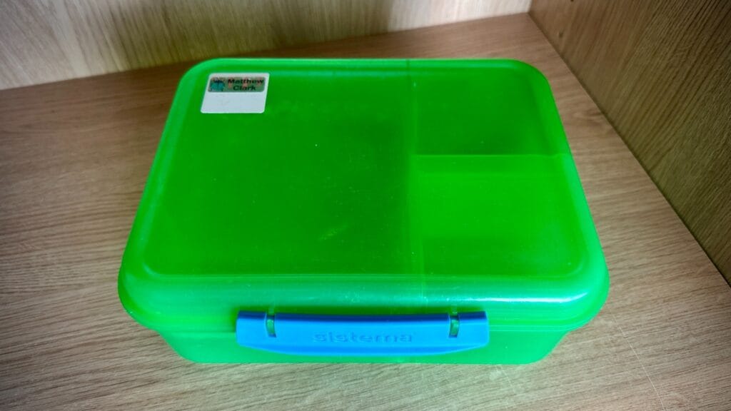 Bright green lunchbox with blue clip photographed on a wooden shelf as part of a lost property collection, circa March, 2026