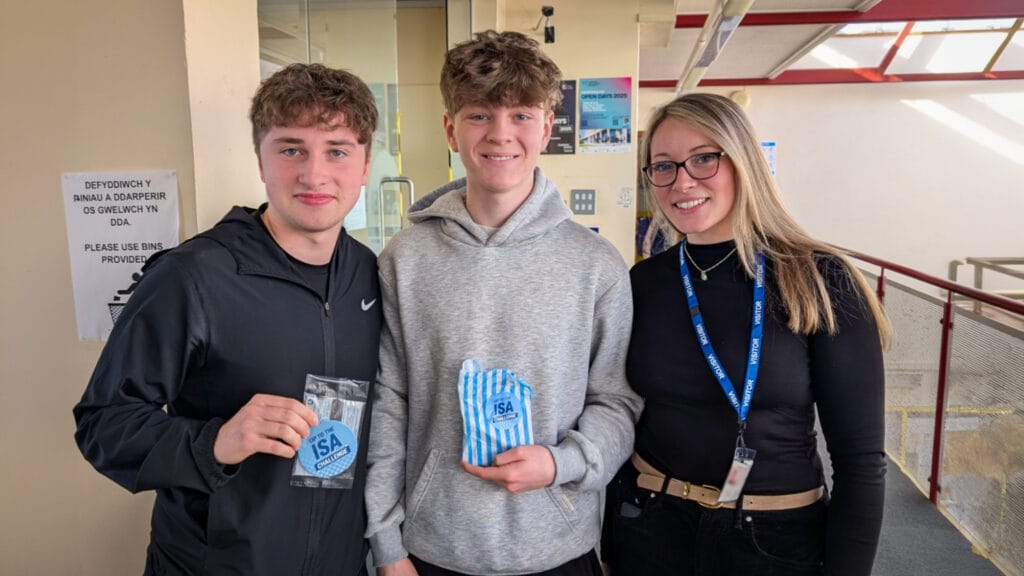 Three people standing together in a school corridor, with two students holding items from the ISA Challenge, circa March, 2026