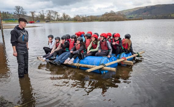 Students sitting on a homemade raft in the lake with an instructor standing nearby, circa March, 2026