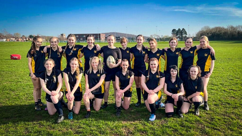 A girls’ rugby team posing together on the school field in team kit, circa March, 2026