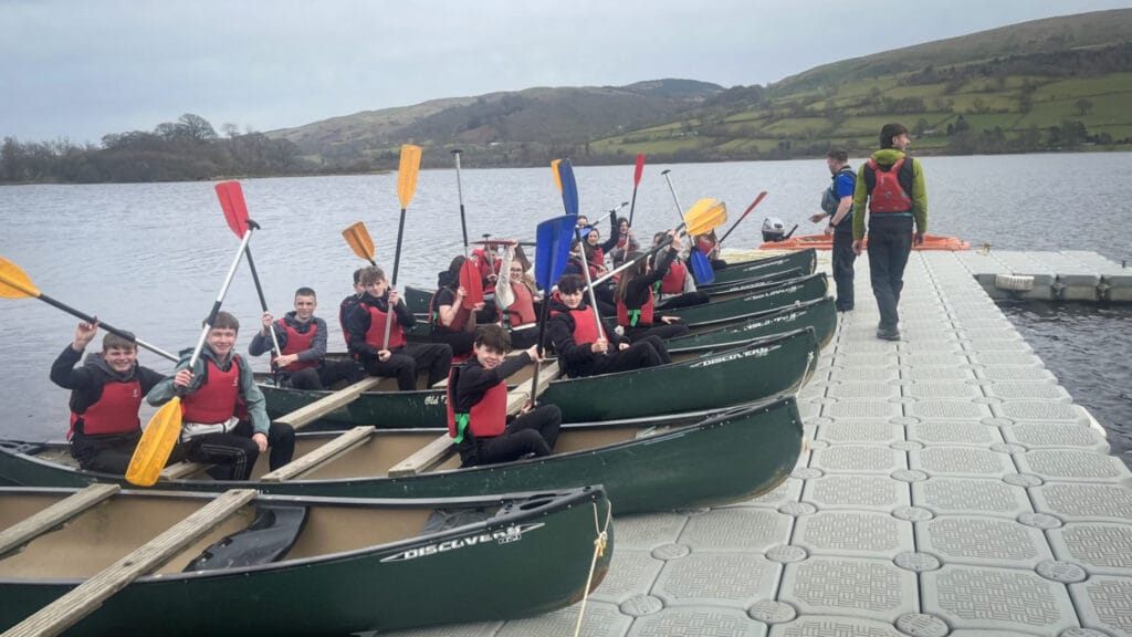 Students sitting in canoes on a lake with paddles raised during an outdoor activity session, circa March, 2026