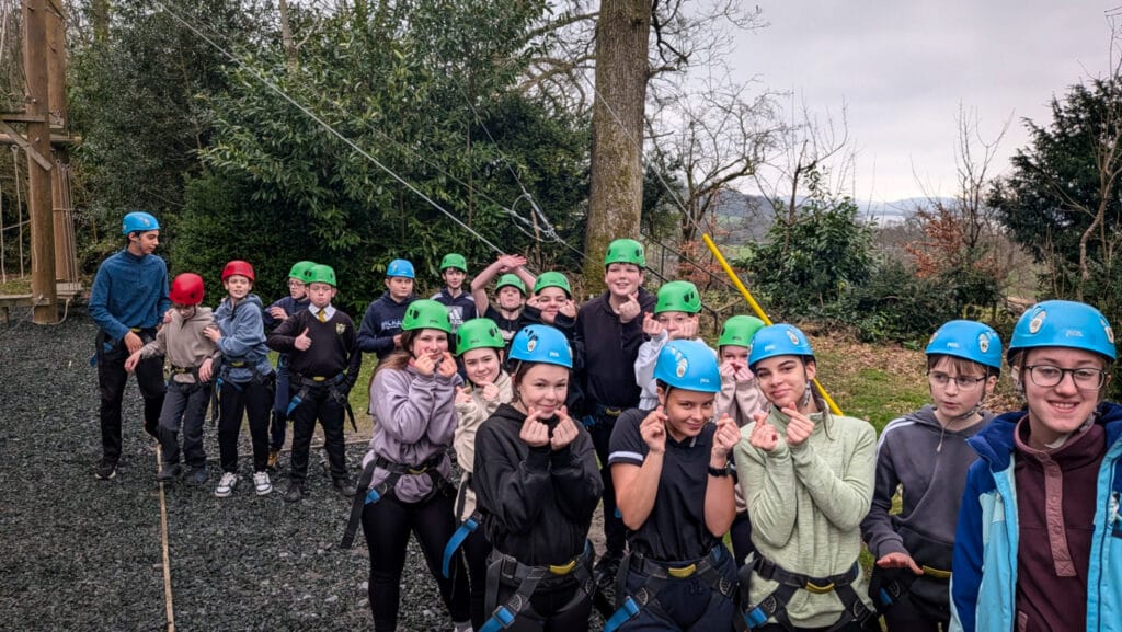 A group of students wearing helmets and harnesses at an outdoor activity centre before starting a climbing or ropes activity, circa March, 2026