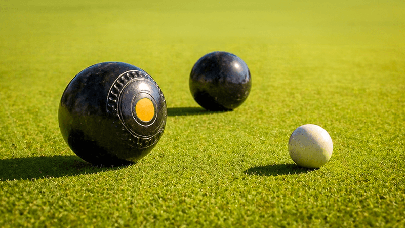 An image of black crown green bowling balls and a white jack resting on a wide, well-kept bowling green