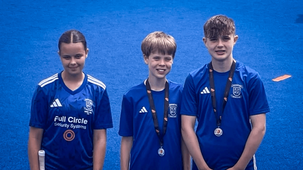 Three students wearing matching blue sports jerseys and medals, standing side by side against a blue background