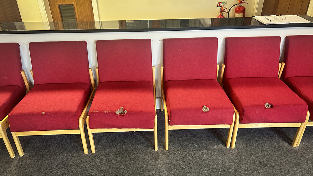 Worn red reception chairs before restoration, showing damaged fabric and torn seat cushions.
