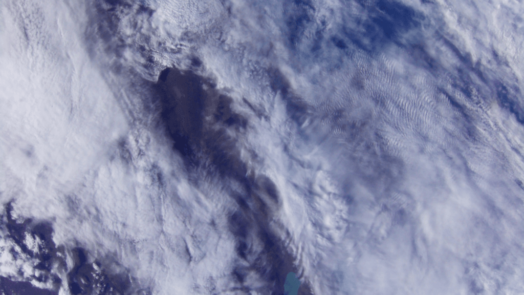 A satellite-style aerial view of clouds swirling over a large body of water, showing varying cloud densities and textures across the scene.