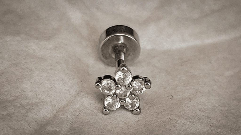 A close-up of a silver flower-shaped stud earring with clear stones, placed on a light textured surface.