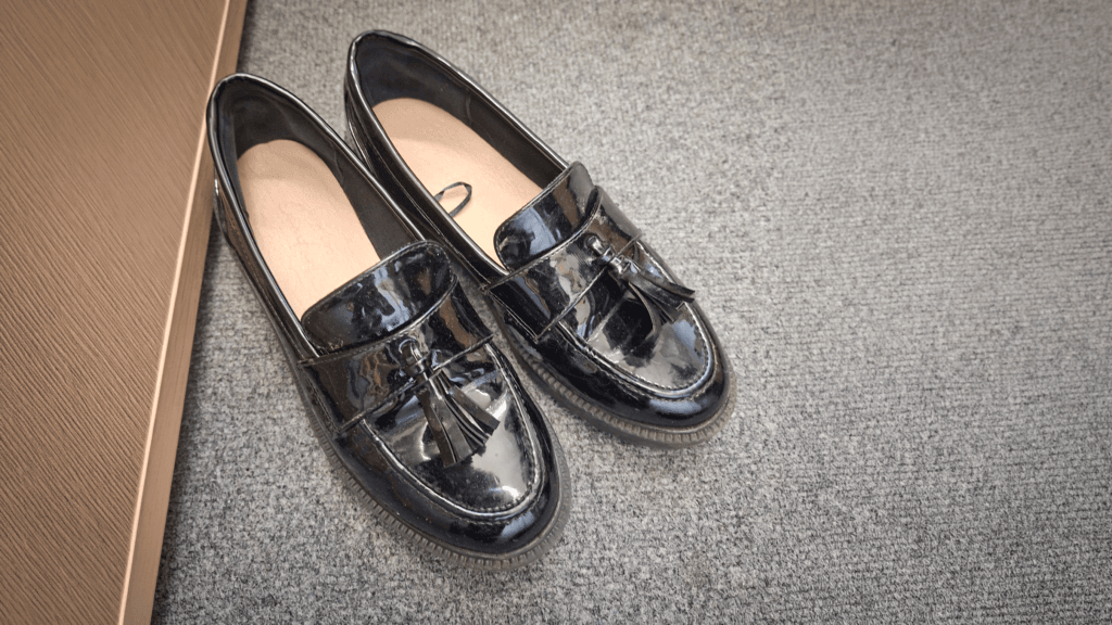 A pair of black school shoes with tassel detailing placed on a grey carpet as part of the school’s lost property collection
