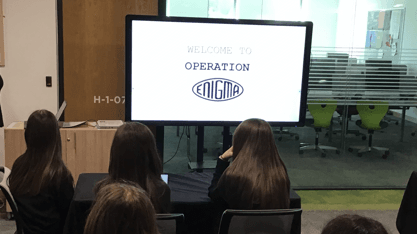 Students watching an Operation Enigma presentation displayed on a large screen.