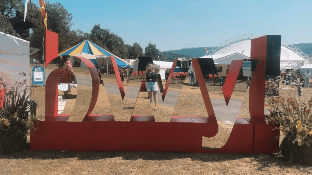 Festival site featuring a large mirrored red sculpture, colourful tents and event marquees.