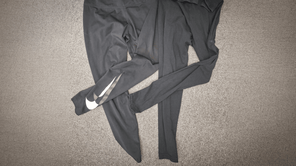 A pair of black Nike leggings with a large white logo on one lower leg, laid out on a grey carpet.