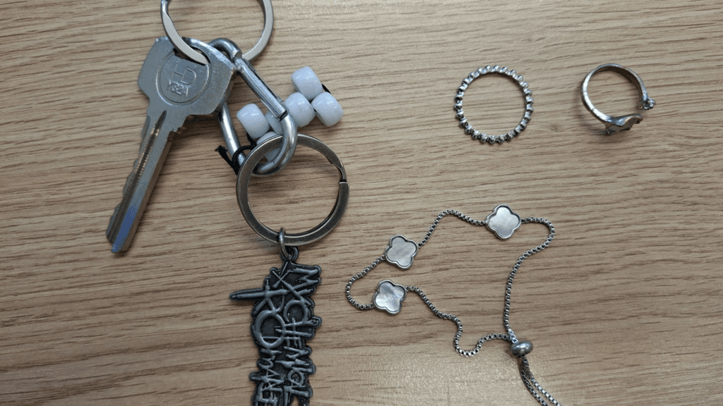 A set of keys, two rings and a silver bracelet arranged on a wooden table.