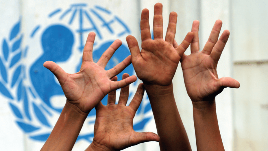 Several raised hands in front of a UNICEF logo, symbolising children’s rights, participation, inclusion, and global support for young people. The background features the blue UNICEF emblem with a globe and laurel design.