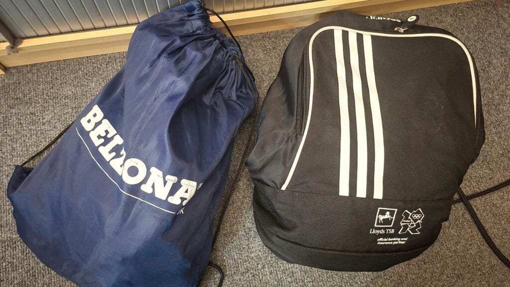 Two sports bags placed on a grey carpet: a blue drawstring bag branded “Bellona” and a black Adidas-style drawstring bag with three white stripes and Lloyds TSB London 2012 Olympics branding.